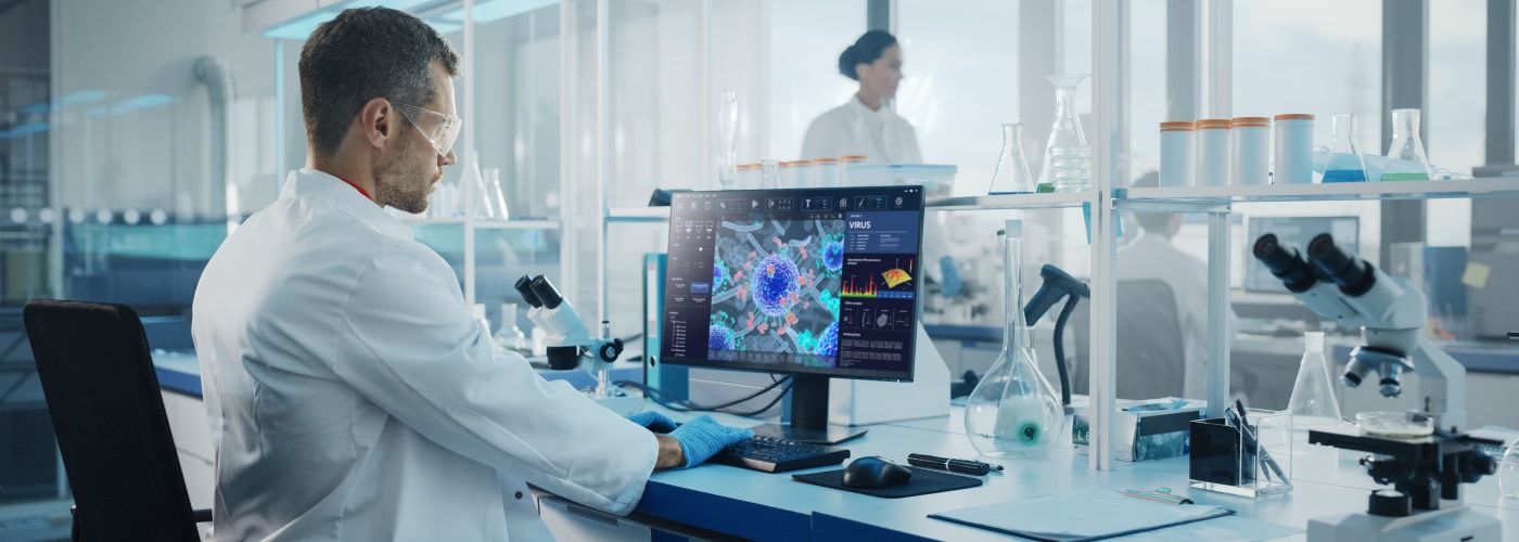 Man in safety goggles sat at a computer screen in a laboratory